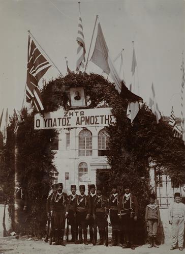Κρήτη, Ηράκλειο. Η τιμητική φρουρά των Κρητών μπροστά από την Ελληνική πρεσβεία. Οι σημαίες της Ελλάδας και των Δυνάμεων, φωτογραφία του Αλέξανδρου Ζαΐμη και πανό με την ένδειξη &quot;ΖΗΤΩ Ο ΑΡΜΟΣΤΗΣ&quot; πάνω από την είσοδο της αυλής. Φωτογραφία, 1907.