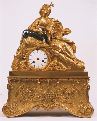 Γαλλικό επιτραπέζιο ρολόι με εκκρεμές από επιχρυσωμένο μπρούντζο κατασκευασμένο από τον οίκο RAINGO FRERES στο Παρίσι το 1841. Είναι διακοσμημένο με μορφή Ελληνίδας, ξαπλωμένης σε ανάκλιντρο. Θέμα διακόσμησης συχνά επαναλαμβανόμενο στα ρολόγια της Εποχής.