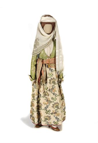 Festal costume from Amorgos. It consists of a silk tunic, a dress, a green silk bodice (&quot;tzaka&quot;) and an emroidered white gossamer kerchief around the waist. The leather slippers are adorned with ribbons. The headgear consists of cotton kerchiefs, 18th cen